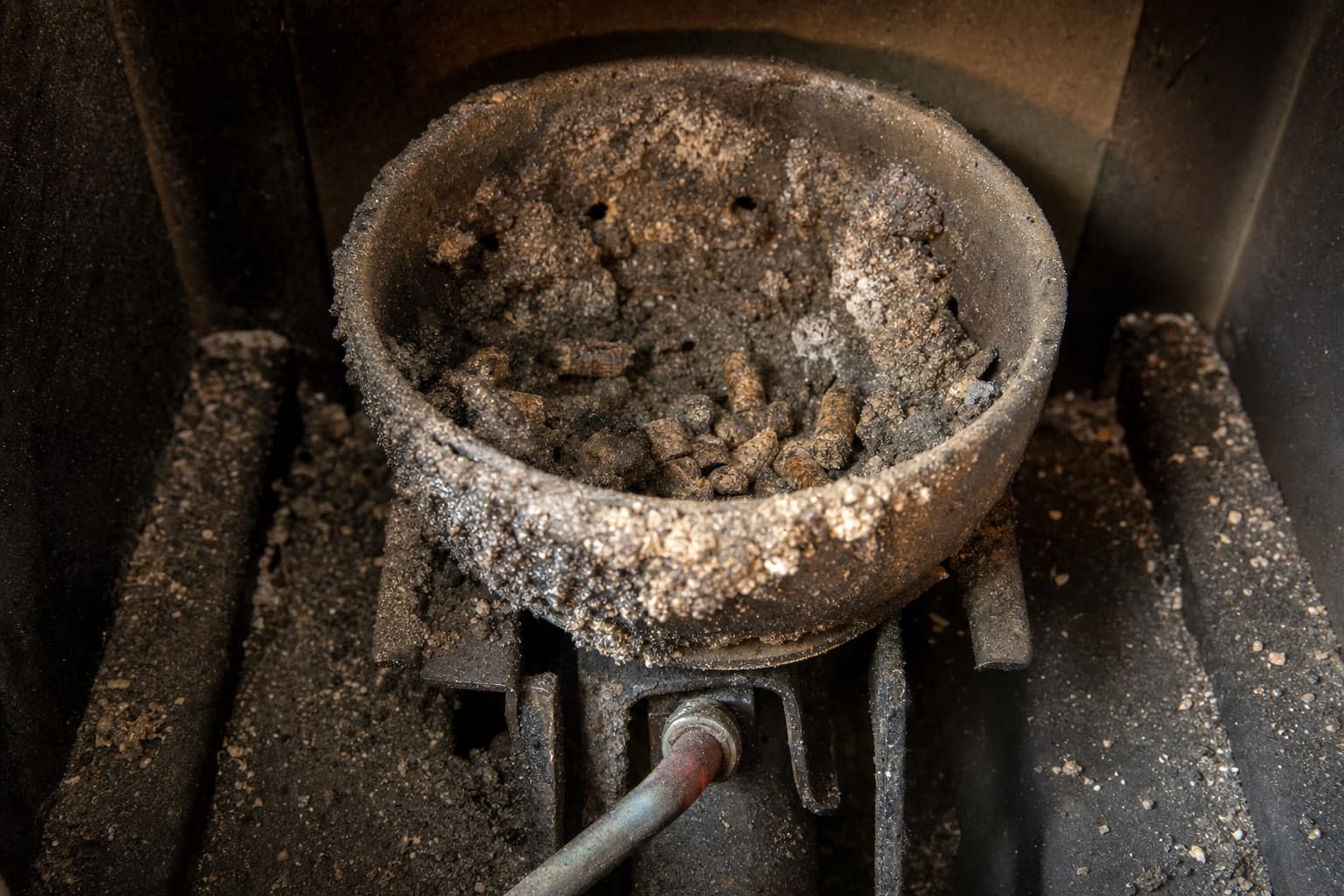 Un creuset fortement encrassé de mâchefer dur et de granulés imbrûlés, la bougie d’allumage visible dessous